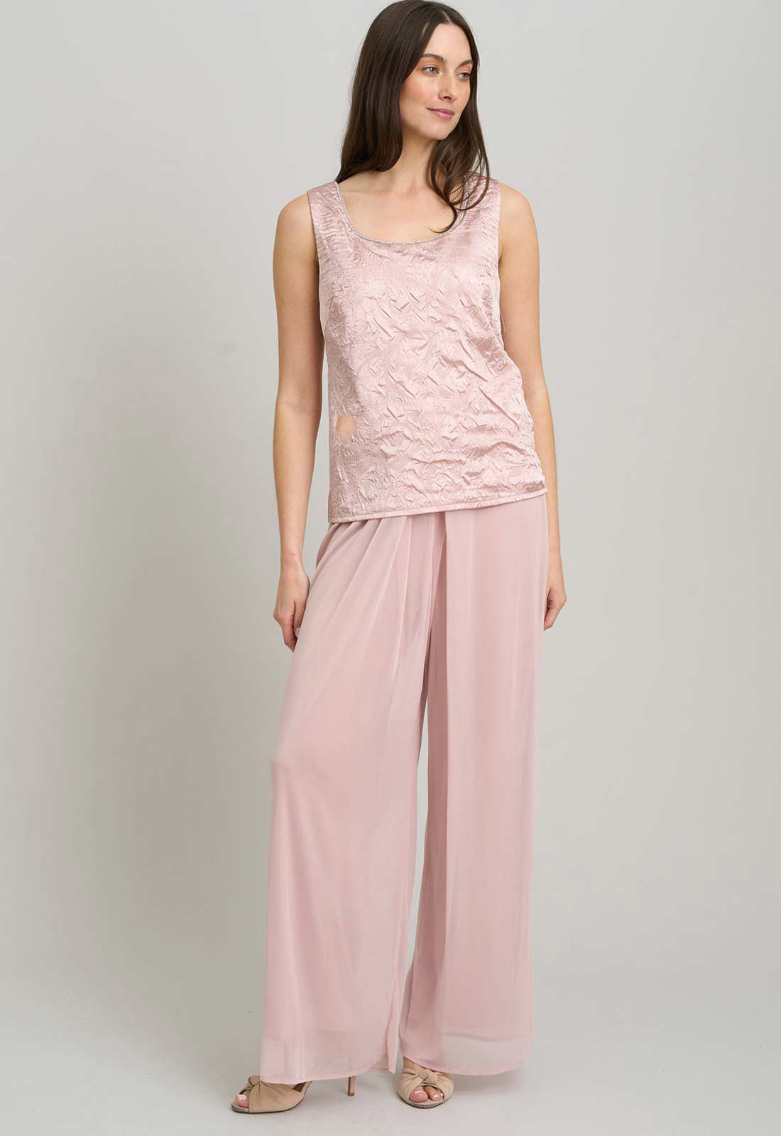 Woman wearing a pink lace top and wide-leg pants on a plain background