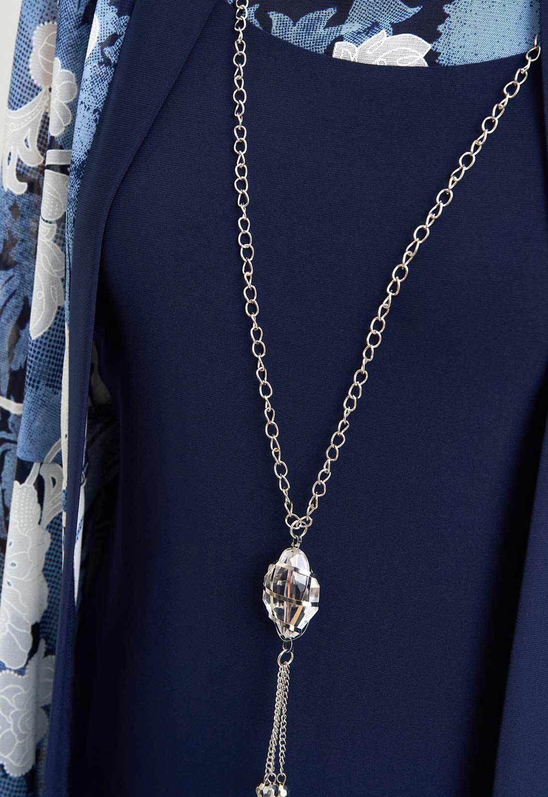 Long silver necklace with a decorative pendant on a dark blue background