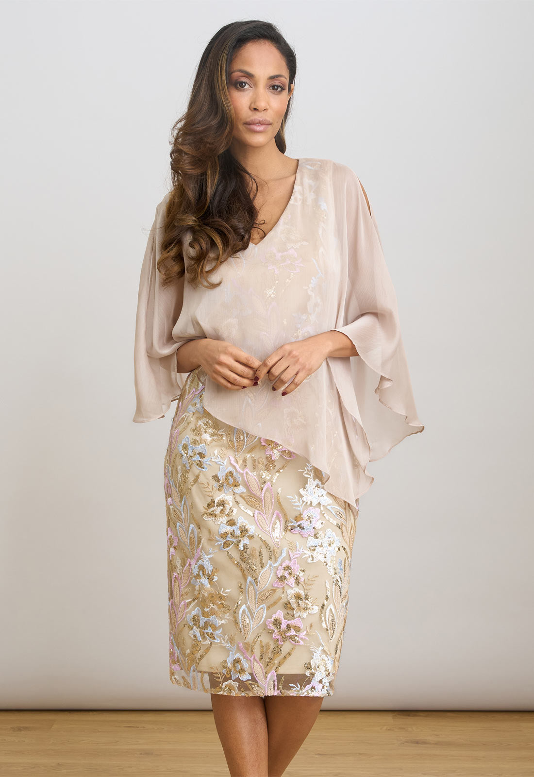Woman wearing a beige floral dress with a matching shawl against a plain background