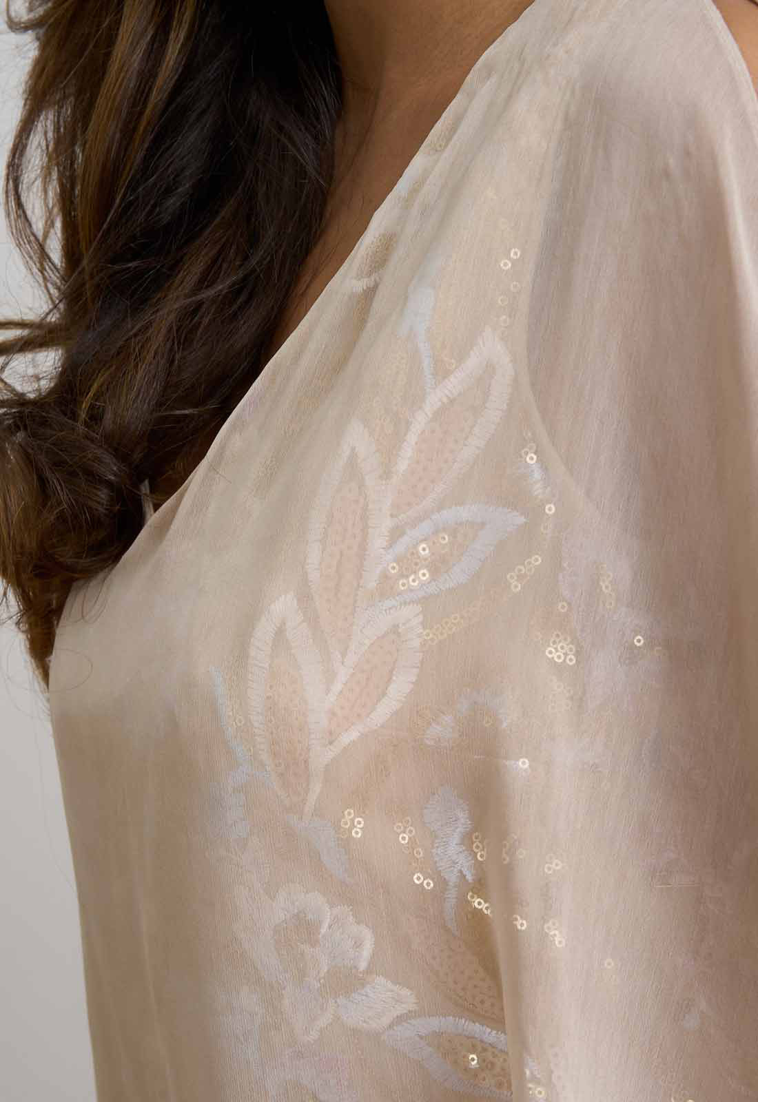 Close-up of a sheer fabric with floral embroidery and sequins on a plain background