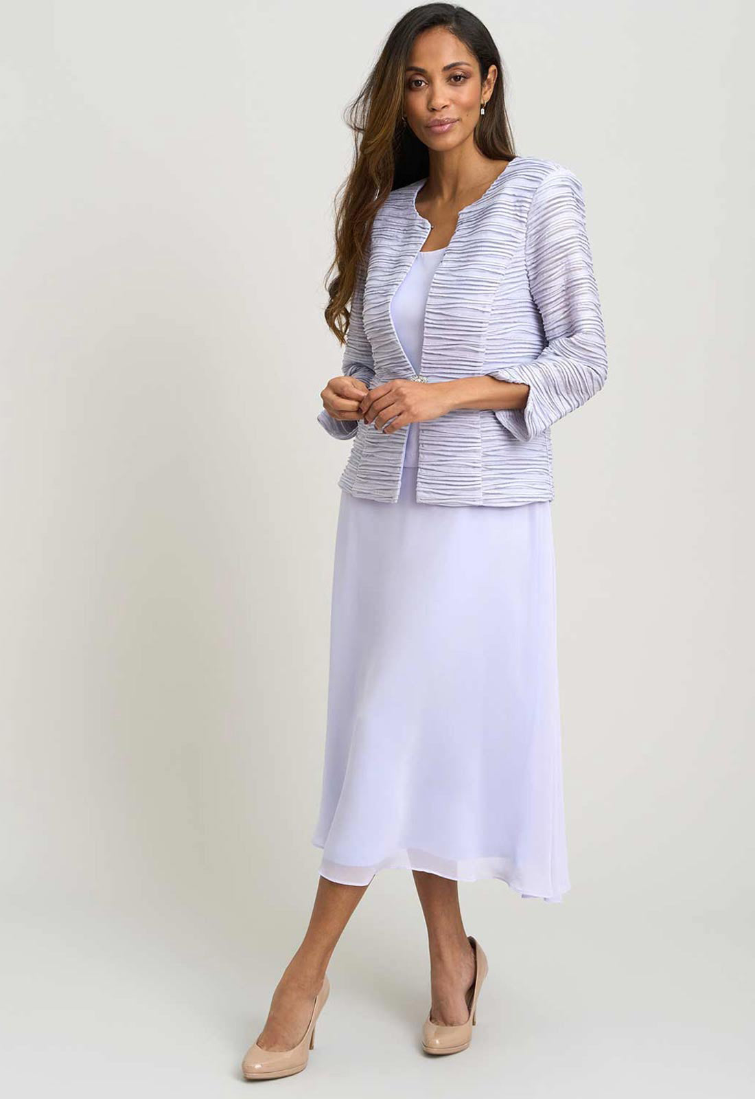 Woman wearing a light purple jacket and white skirt on a plain background