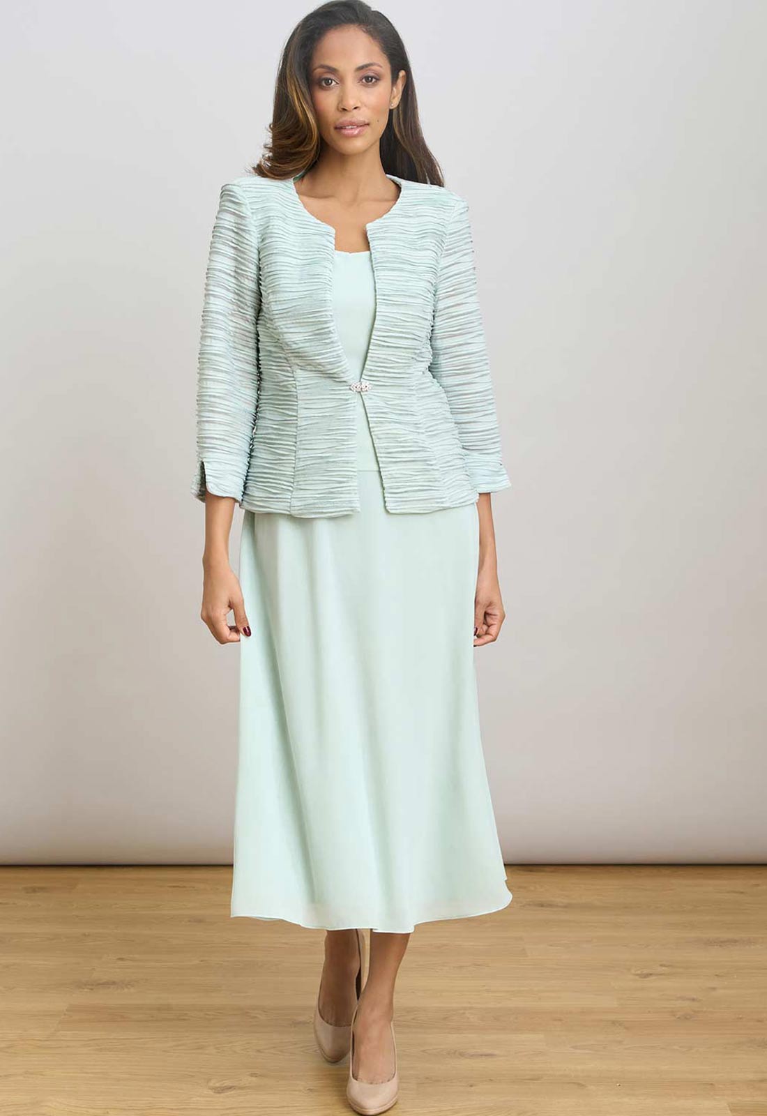 Woman wearing a light green suit with a jacket and skirt on a plain background