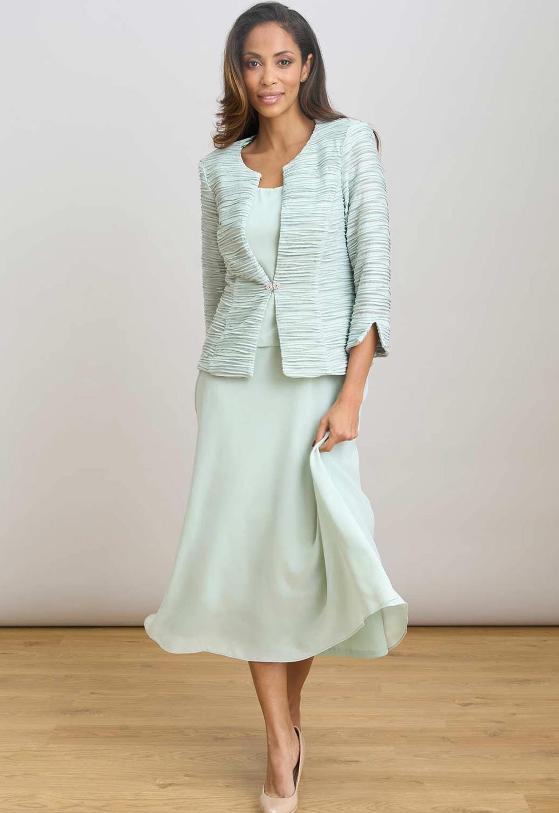Woman wearing a light green dress with a matching jacket on a plain background
