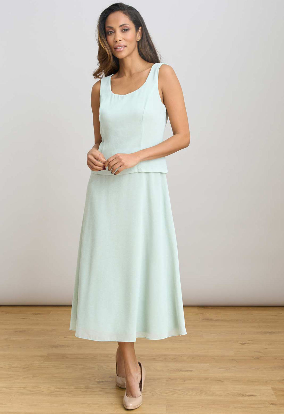Woman wearing a light green sleeveless dress on a plain background
