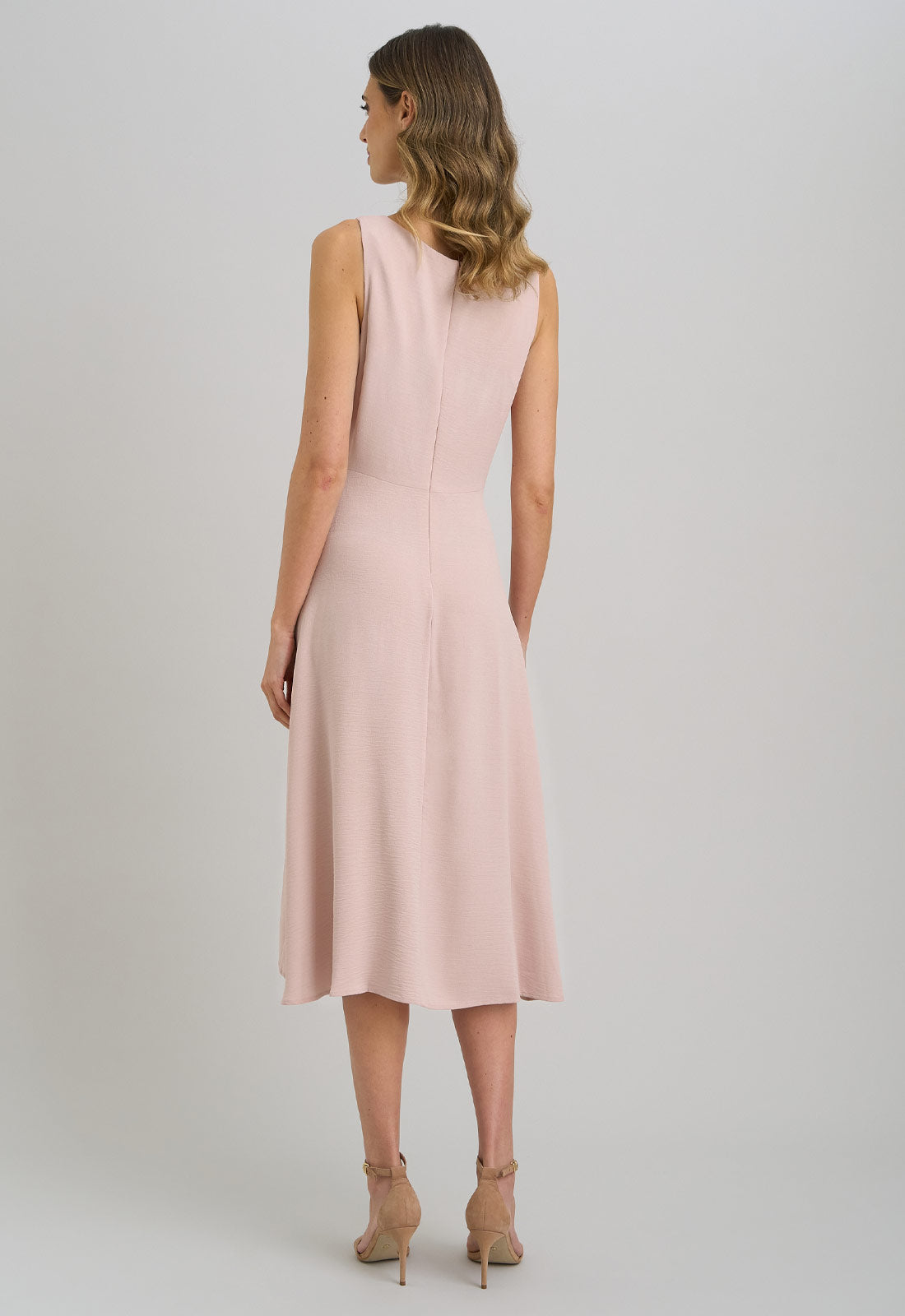 Woman wearing a light pink sleeveless dress on a plain background