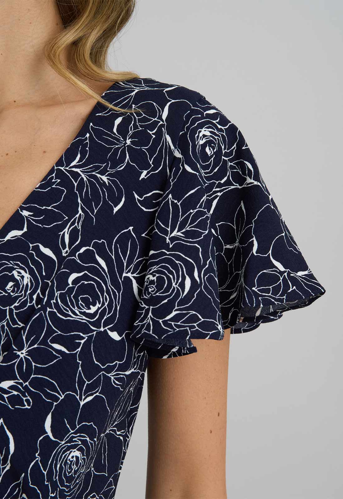 Navy blue blouse with white floral pattern worn by a person on a gray background
