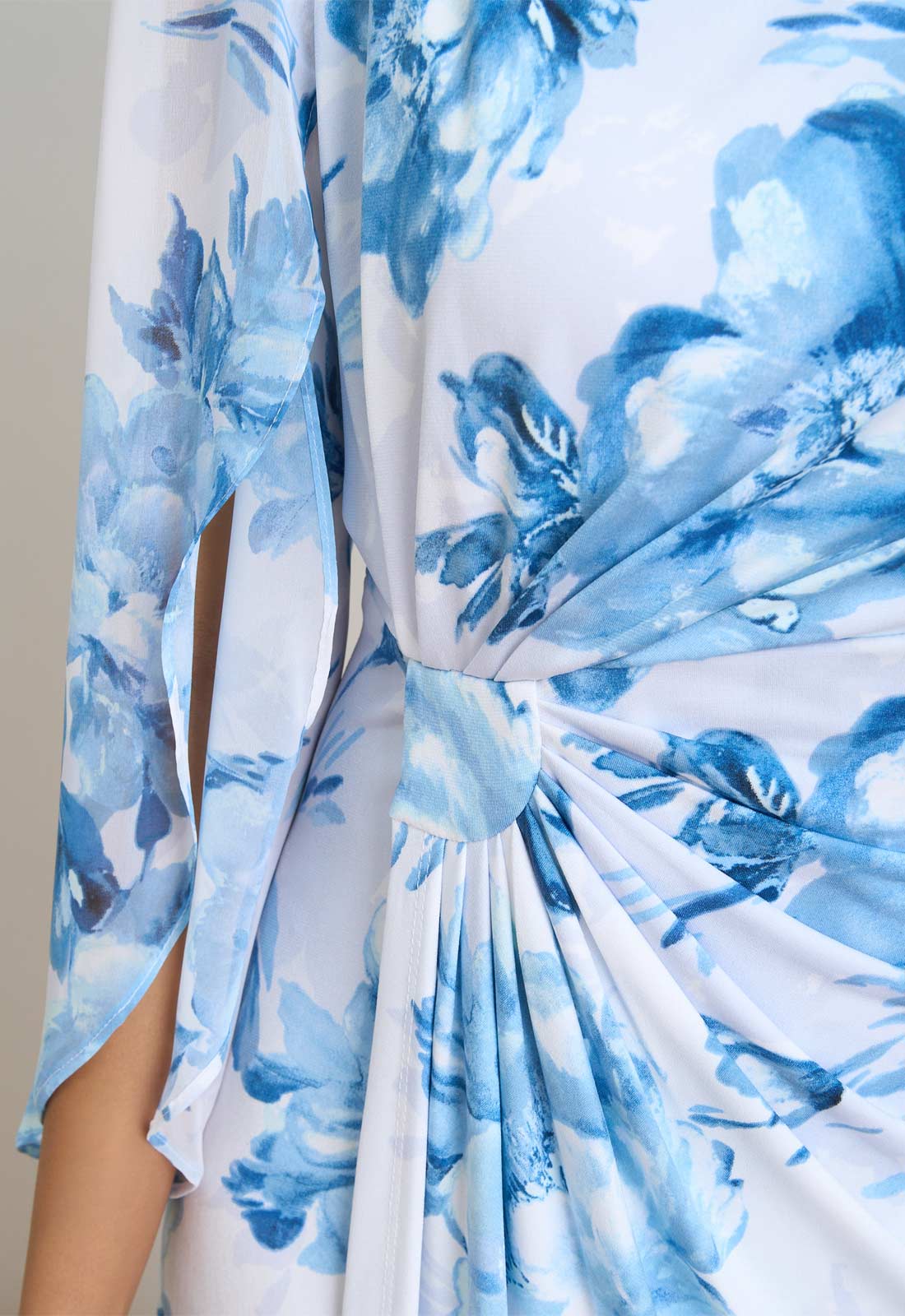 Close-up of a blue floral dress with a knot detail on a plain background