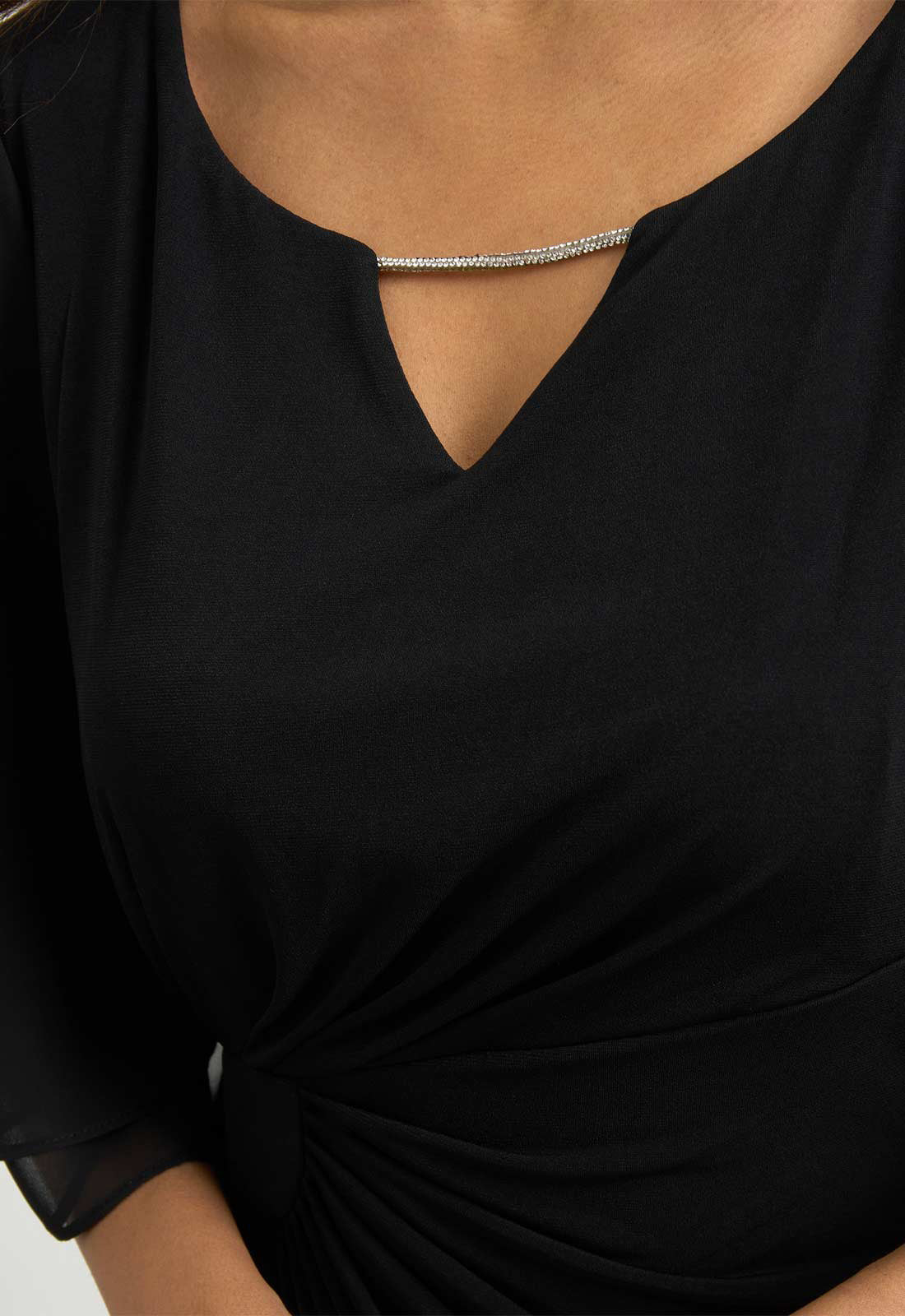 Close-up of a person wearing a black top with a V-neck and a knot detail.