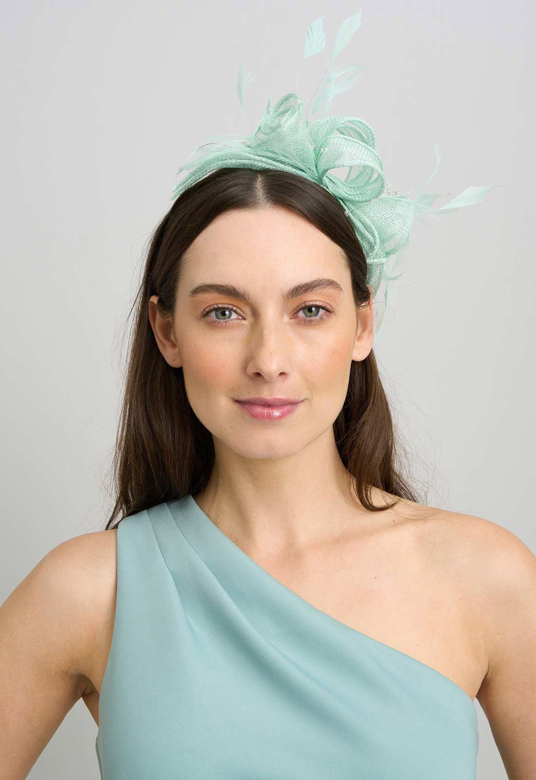 Woman wearing a light green fascinator with feathers on a plain background
