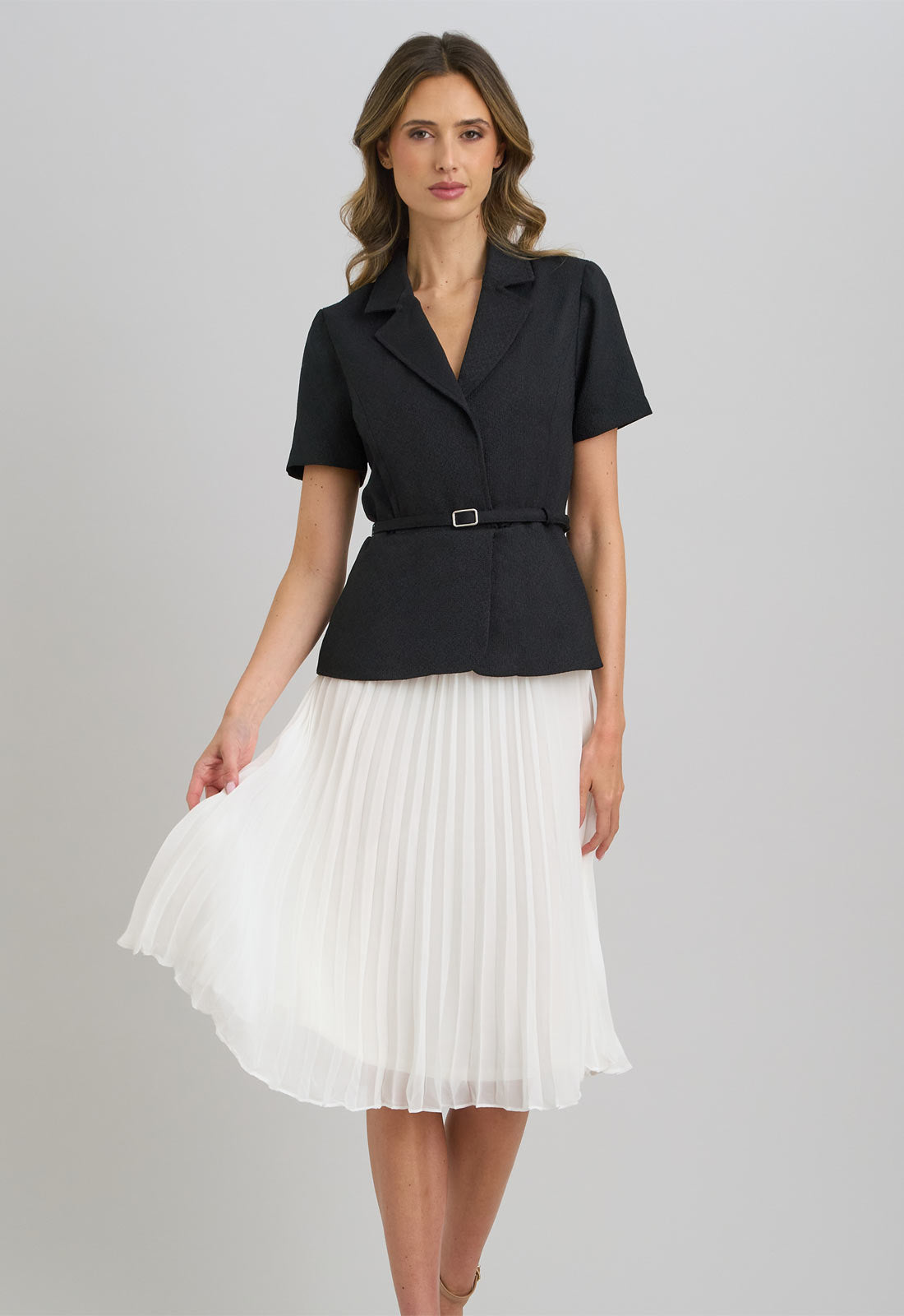 Woman wearing a black top and white pleated skirt on a gray background