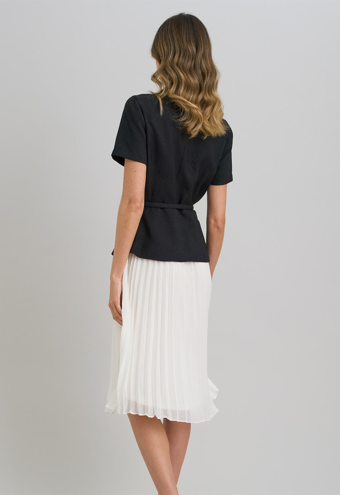 Woman wearing a black top and white pleated skirt on a gray background