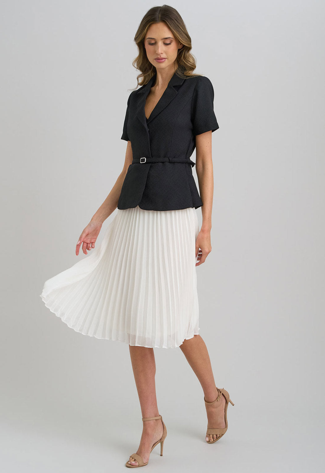 Woman wearing a black blazer and white pleated skirt on a gray background