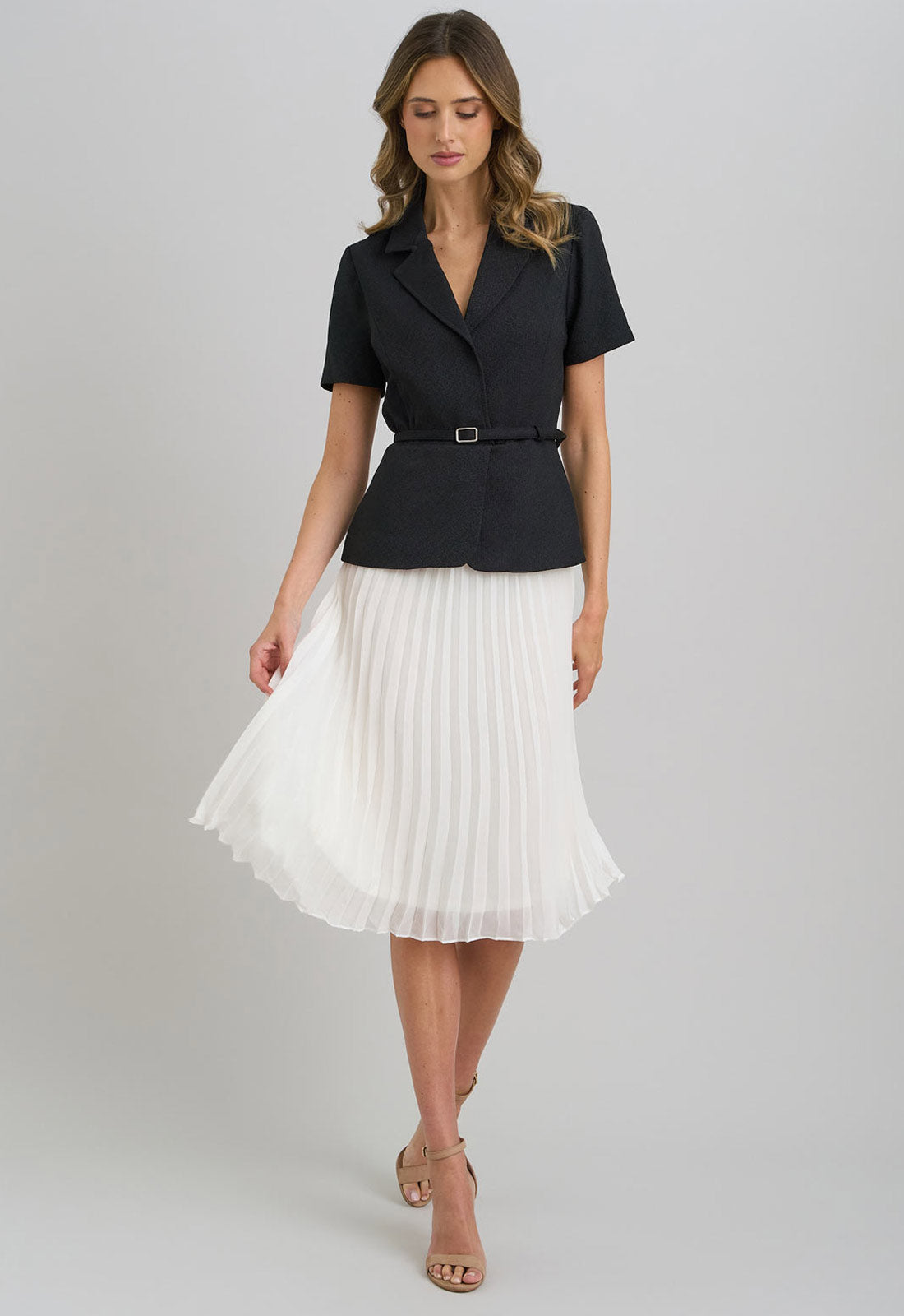 Woman wearing a black top and white pleated skirt on a gray background