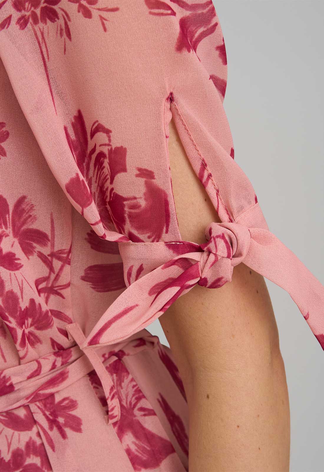 Close-up of a pink floral dress with a knot detail on a plain background