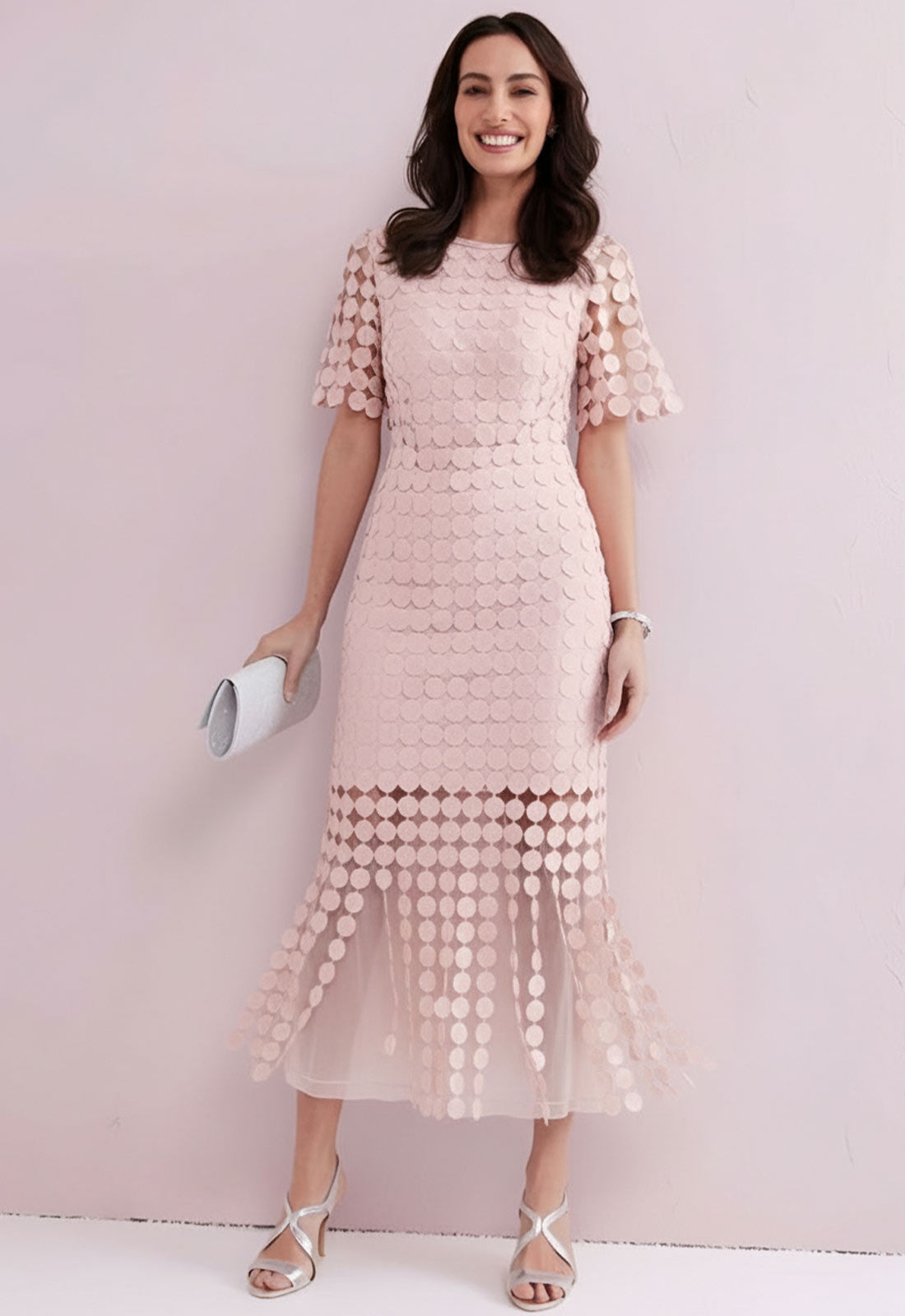 Woman wearing a light pink dress with a patterned design against a plain background