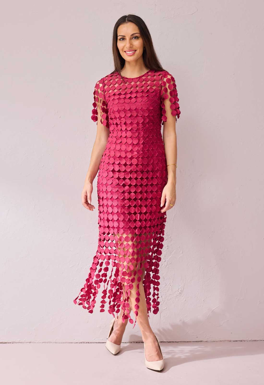 Woman wearing a pink dress with cut-out patterns on a plain background