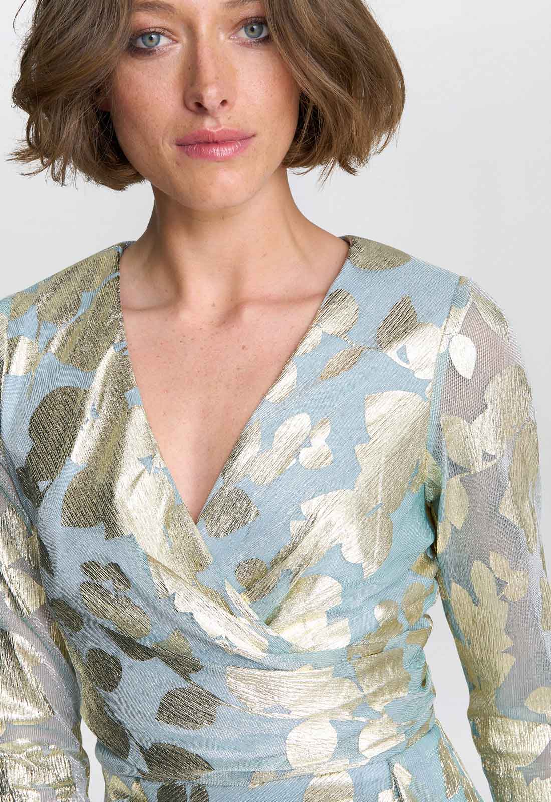 Woman wearing a light blue dress with gold and white abstract patterns on a plain background