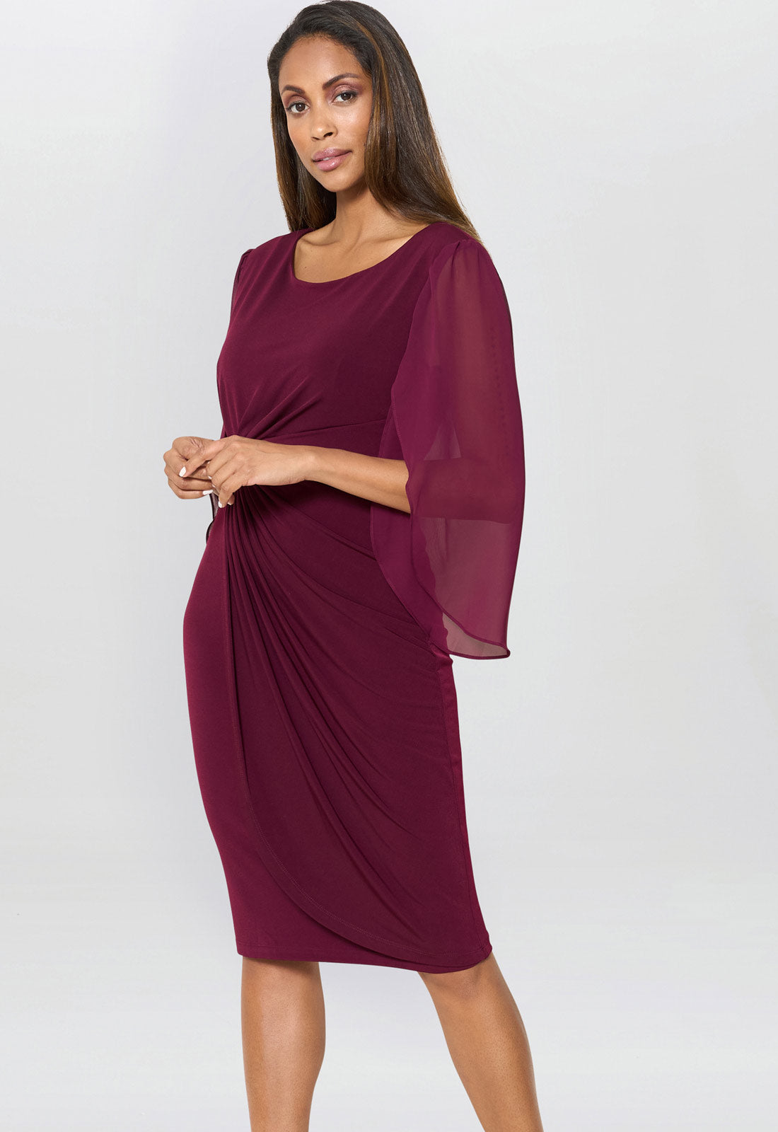 Woman wearing a burgundy dress with sheer sleeves on a white background