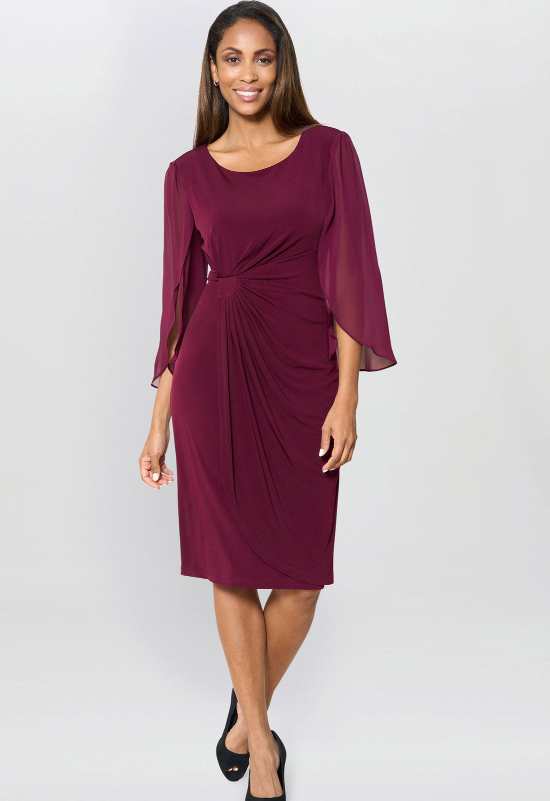 Woman wearing a burgundy dress with cape sleeves on a white background