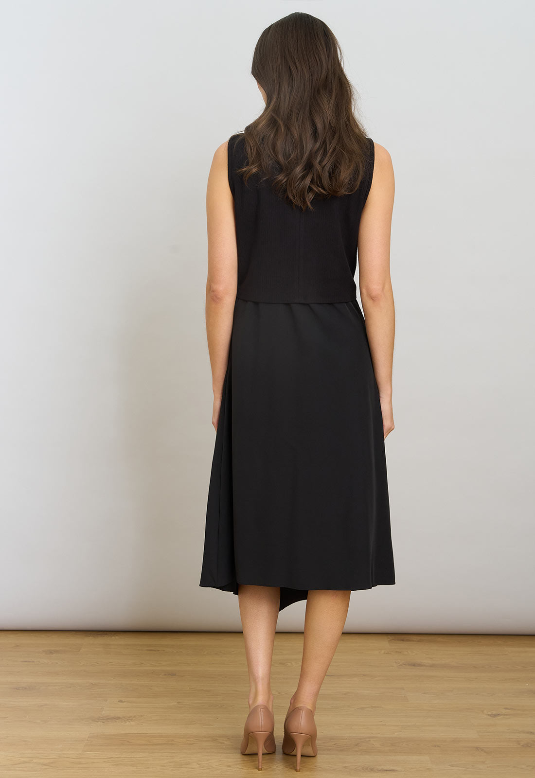 Woman wearing a black sleeveless dress against a white wall.