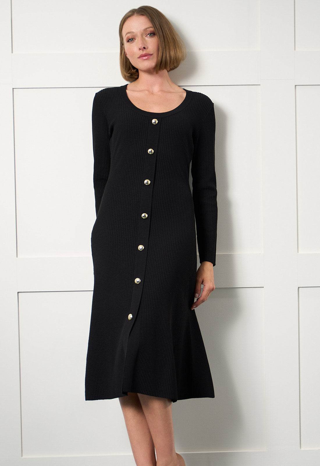Woman wearing a black dress with silver buttons against a white wall
