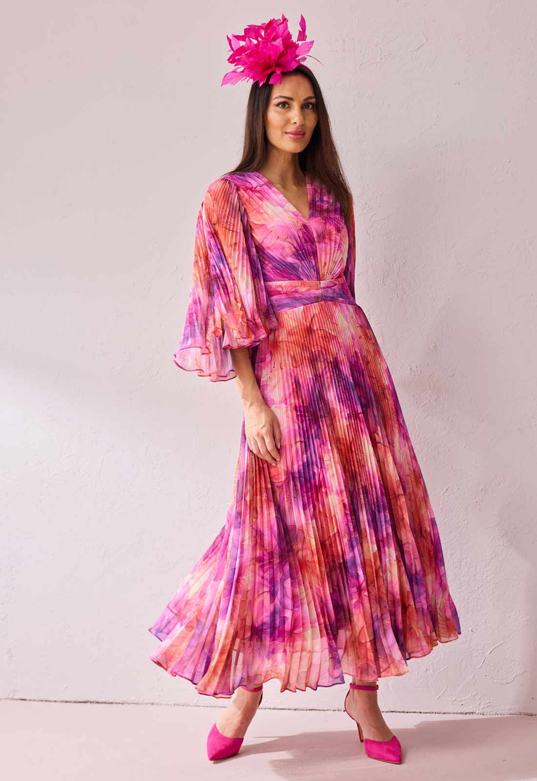 Woman wearing a colorful tie-dye dress with a pink floral headpiece against a white background