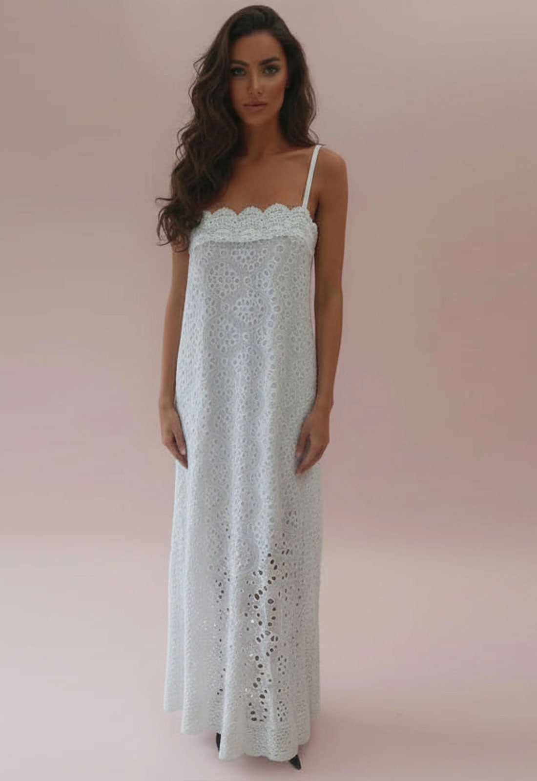 Woman wearing a white lace dress against a pink background