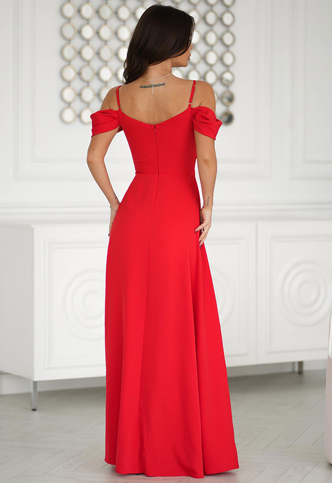 Woman wearing a red evening gown in a room with white walls and decorative elements.