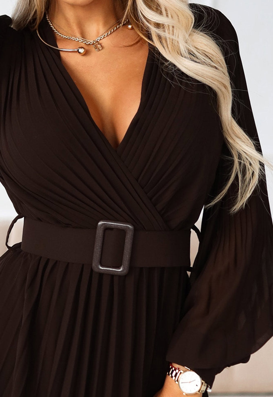 Black dress with a belt and a watch on a neutral background