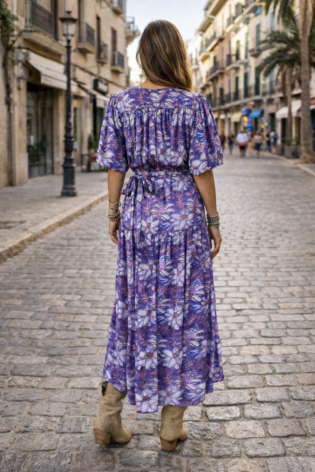 Woman in a purple floral dress walking down a sunlit street.