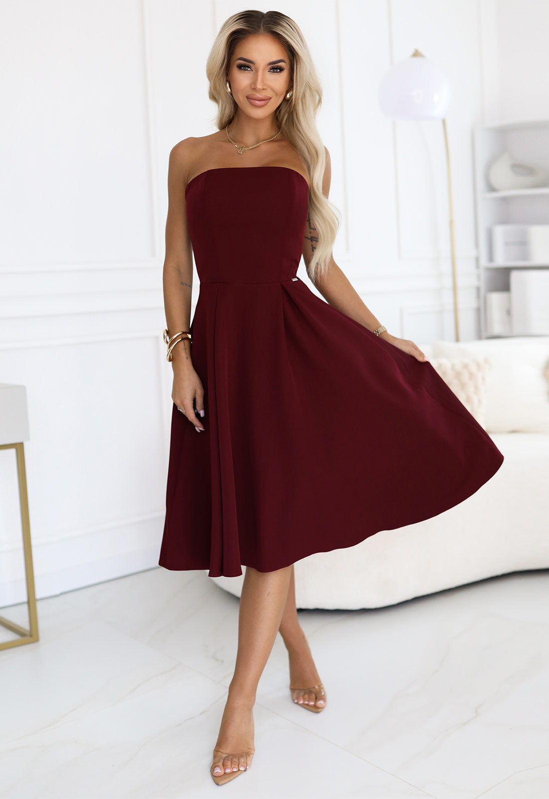 Woman wearing a burgundy strapless dress in a minimalistic room.