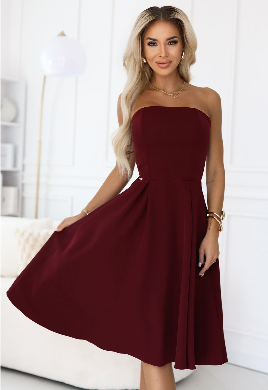 Woman wearing a burgundy strapless dress in a bright room.