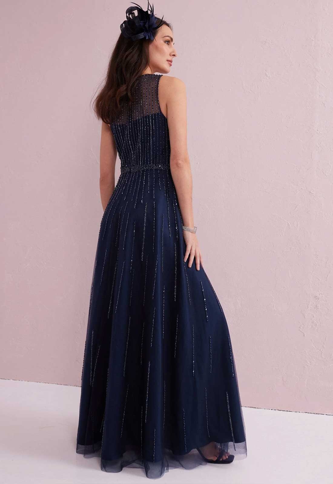 Woman wearing a navy blue evening gown with a floral headpiece against a pink background