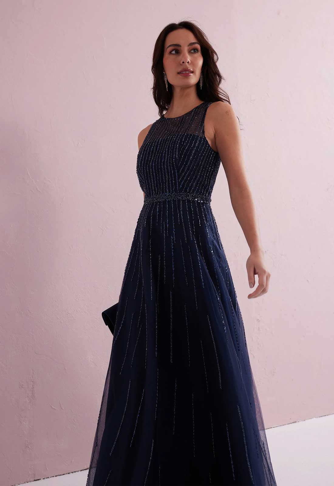 Woman wearing a dark blue evening gown against a light pink background