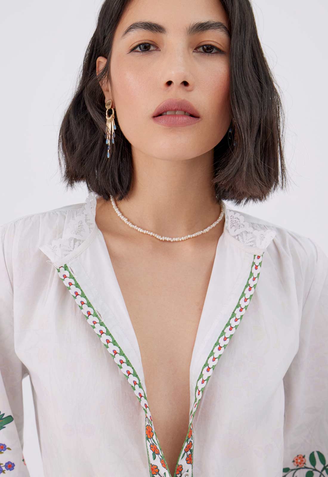 Woman wearing a white blouse with floral embroidery on a plain background