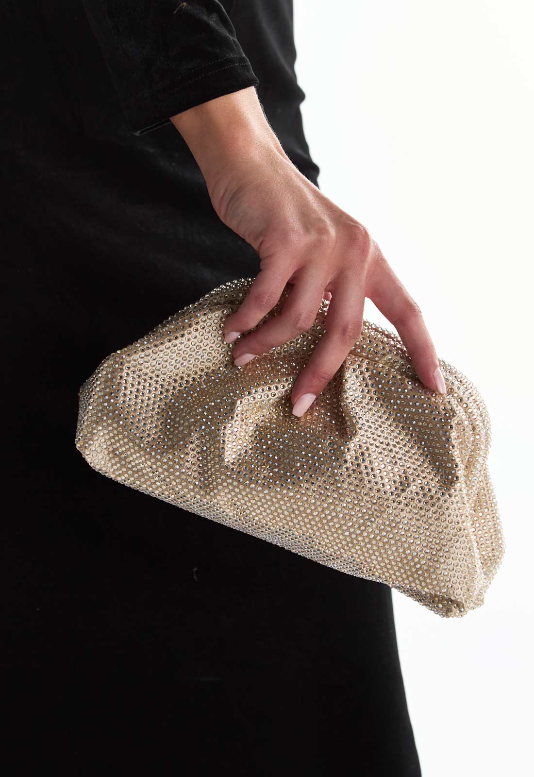Gold clutch held by a person against a black background