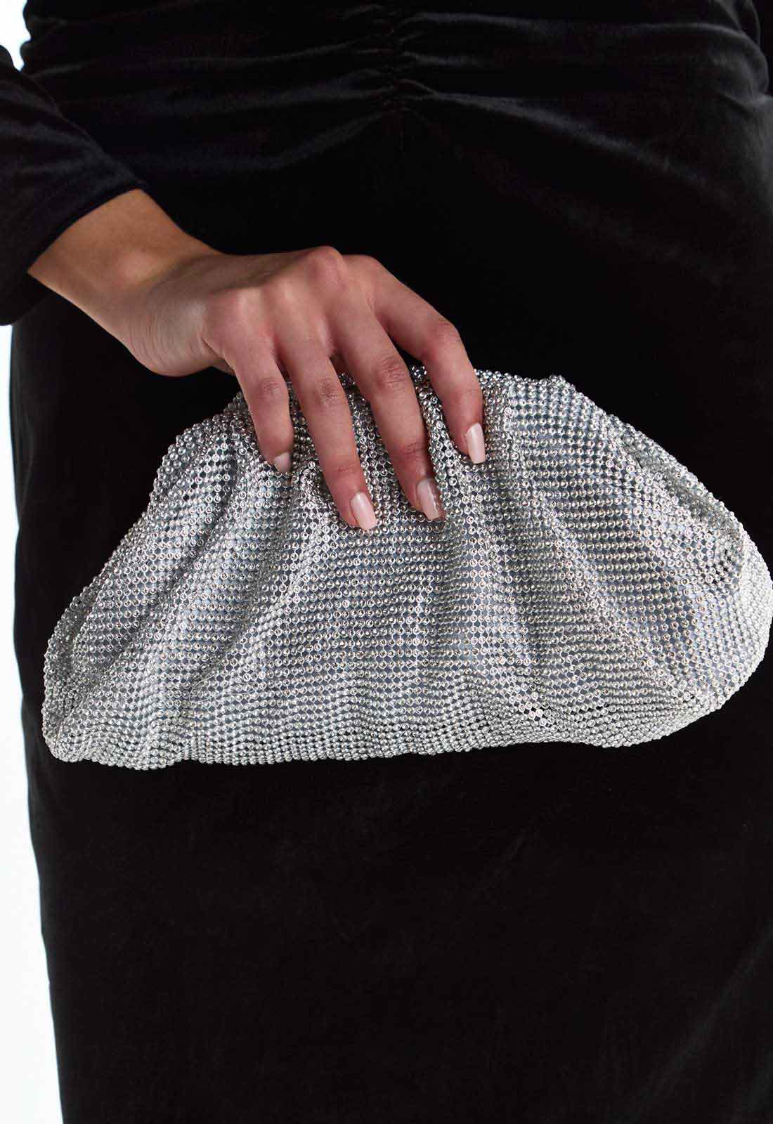 Silver clutch held by a hand against a black background