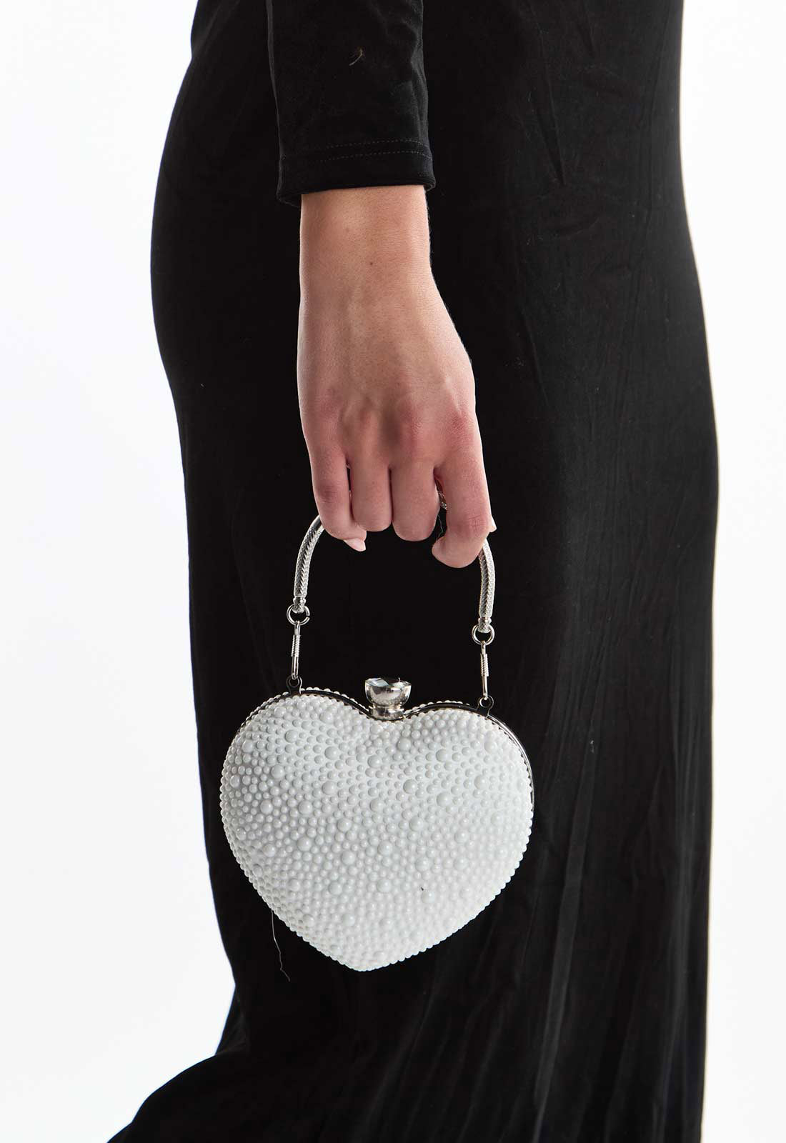 Heart-shaped white clutch held by a person wearing a black dress.