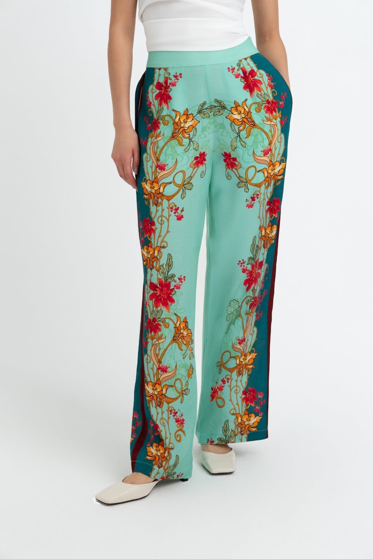 Teal pants with colorful floral embroidery worn by a person on a white background