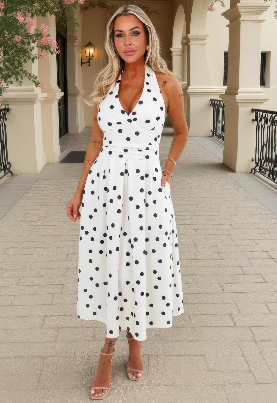 Woman wearing a white dress with black polka dots in an outdoor setting.