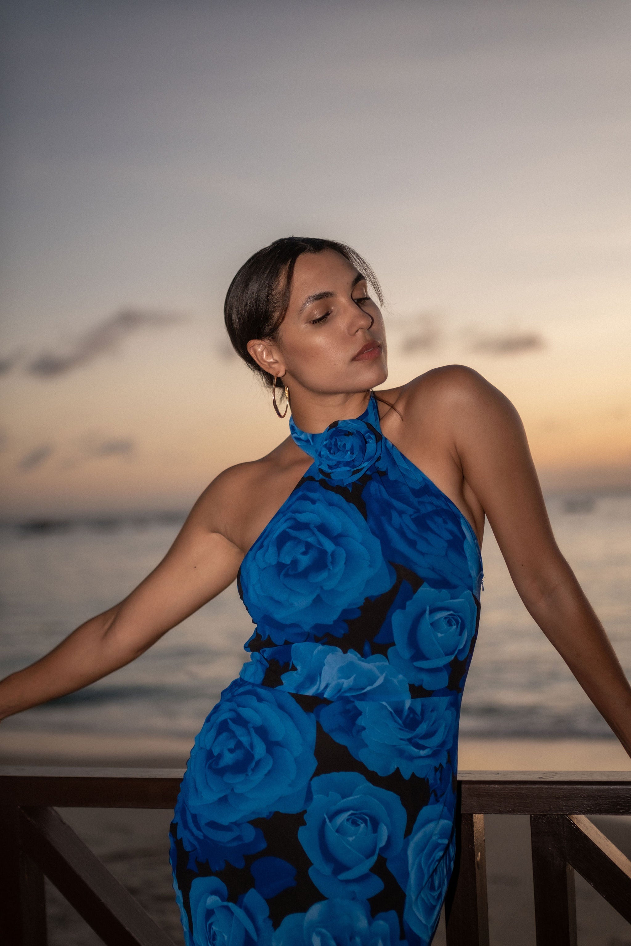 Woman in a blue floral dress standing by the ocean at sunset