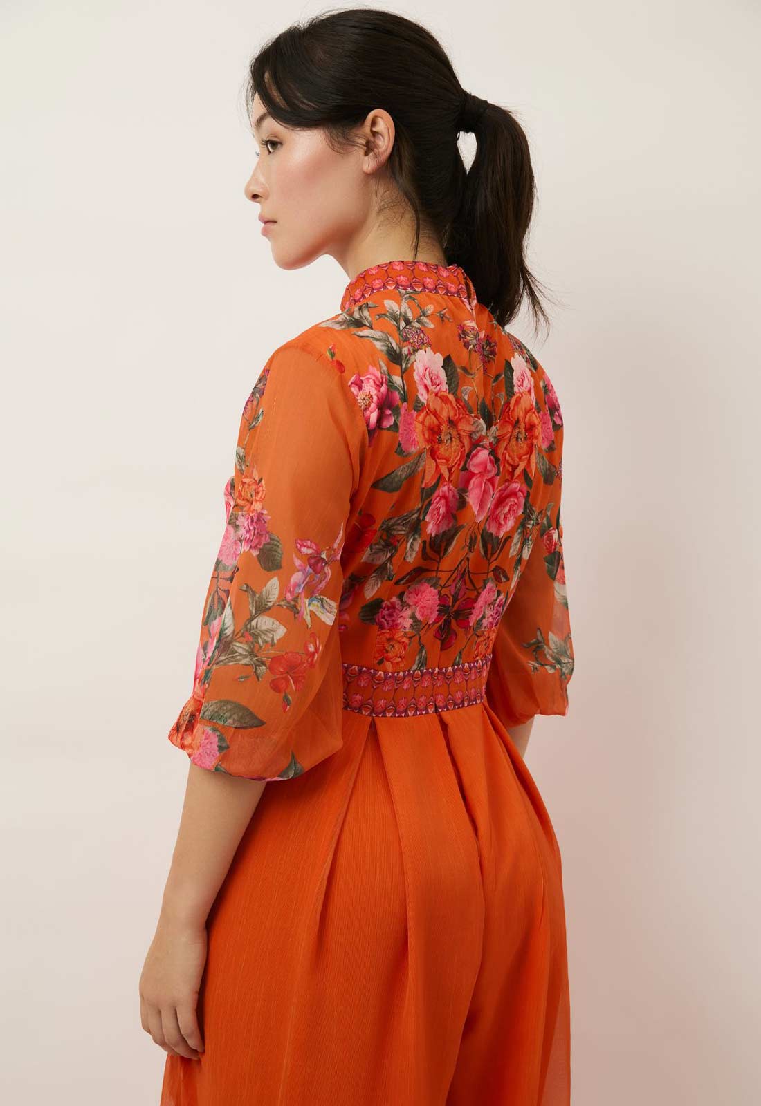 Woman wearing an orange floral dress against a plain background