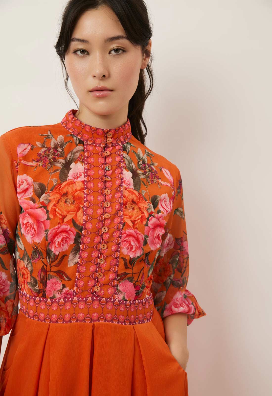 Woman wearing an orange floral embroidered top against a plain background