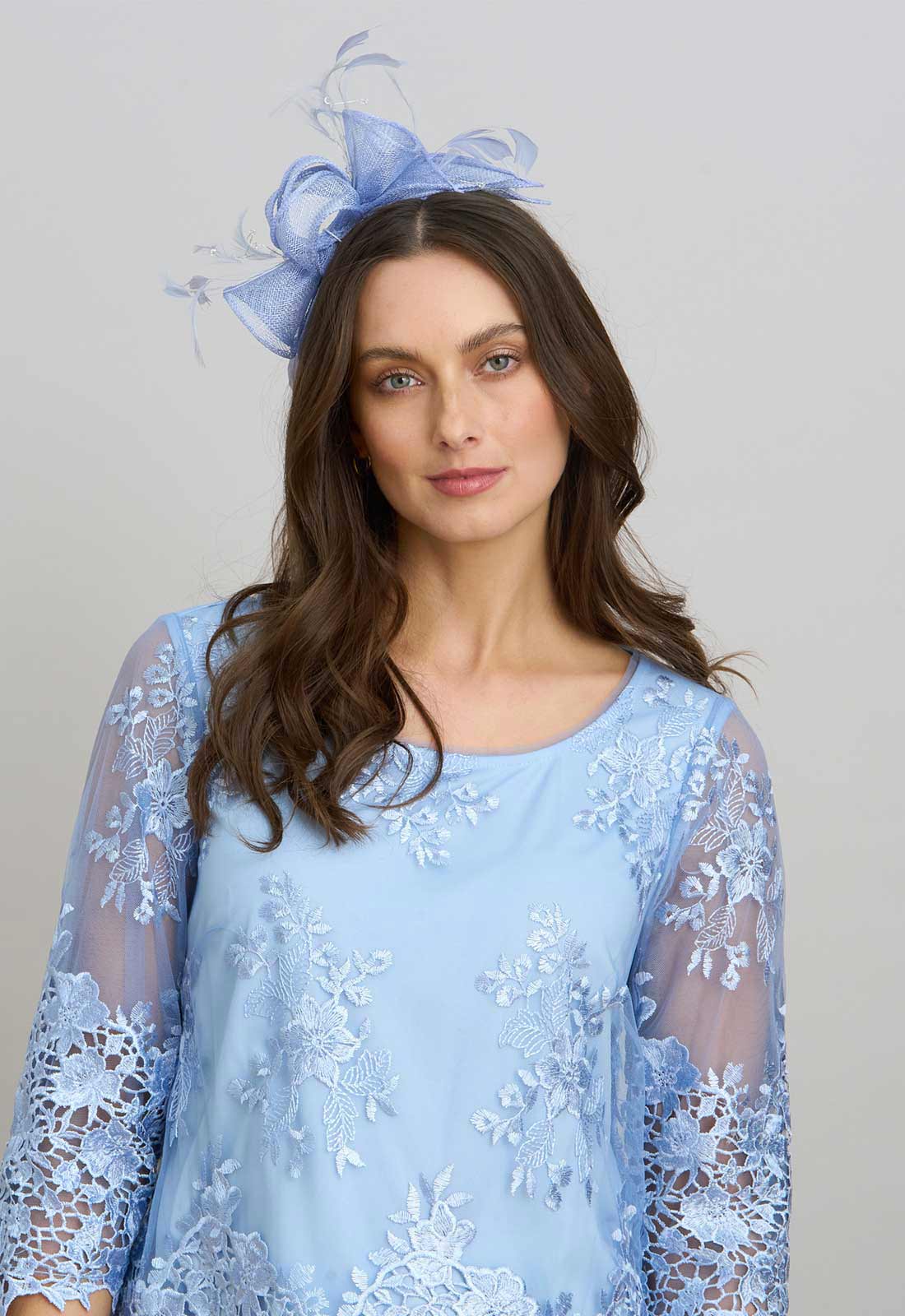 Woman wearing a light blue lace dress with a matching headpiece against a plain background
