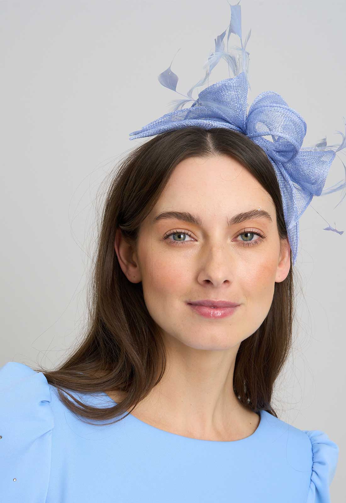 Woman wearing a blue decorative headpiece against a light gray background