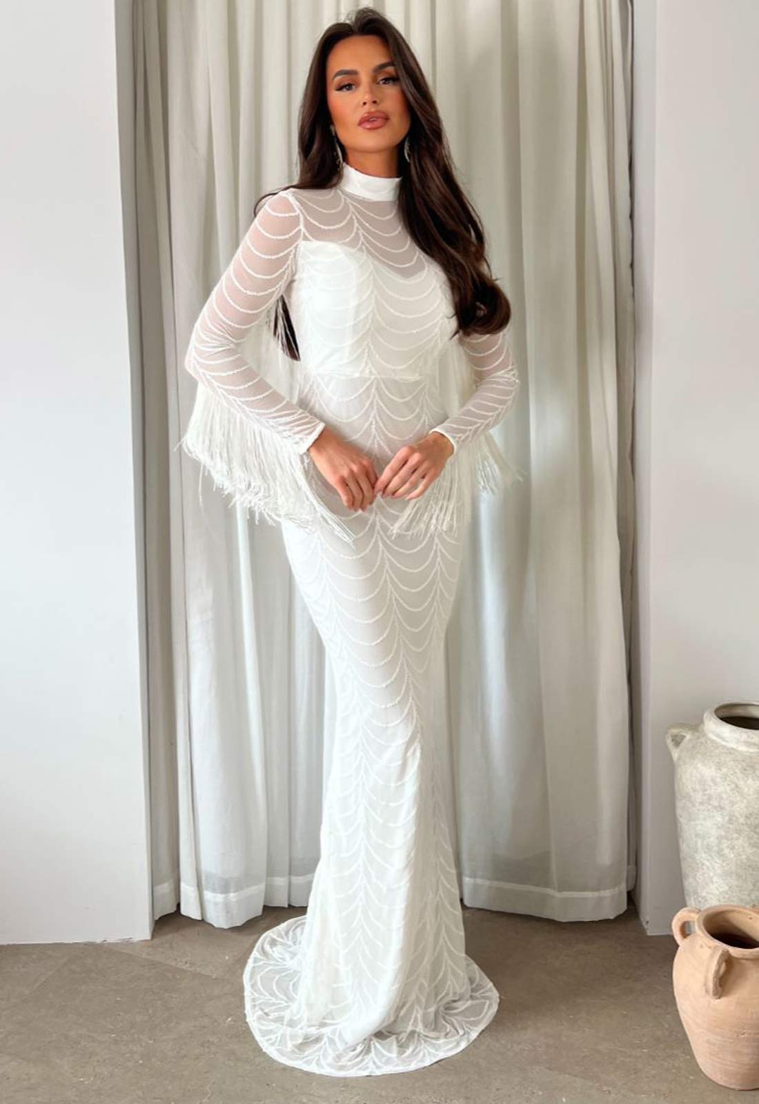Woman wearing a white lace dress standing in front of a curtain.