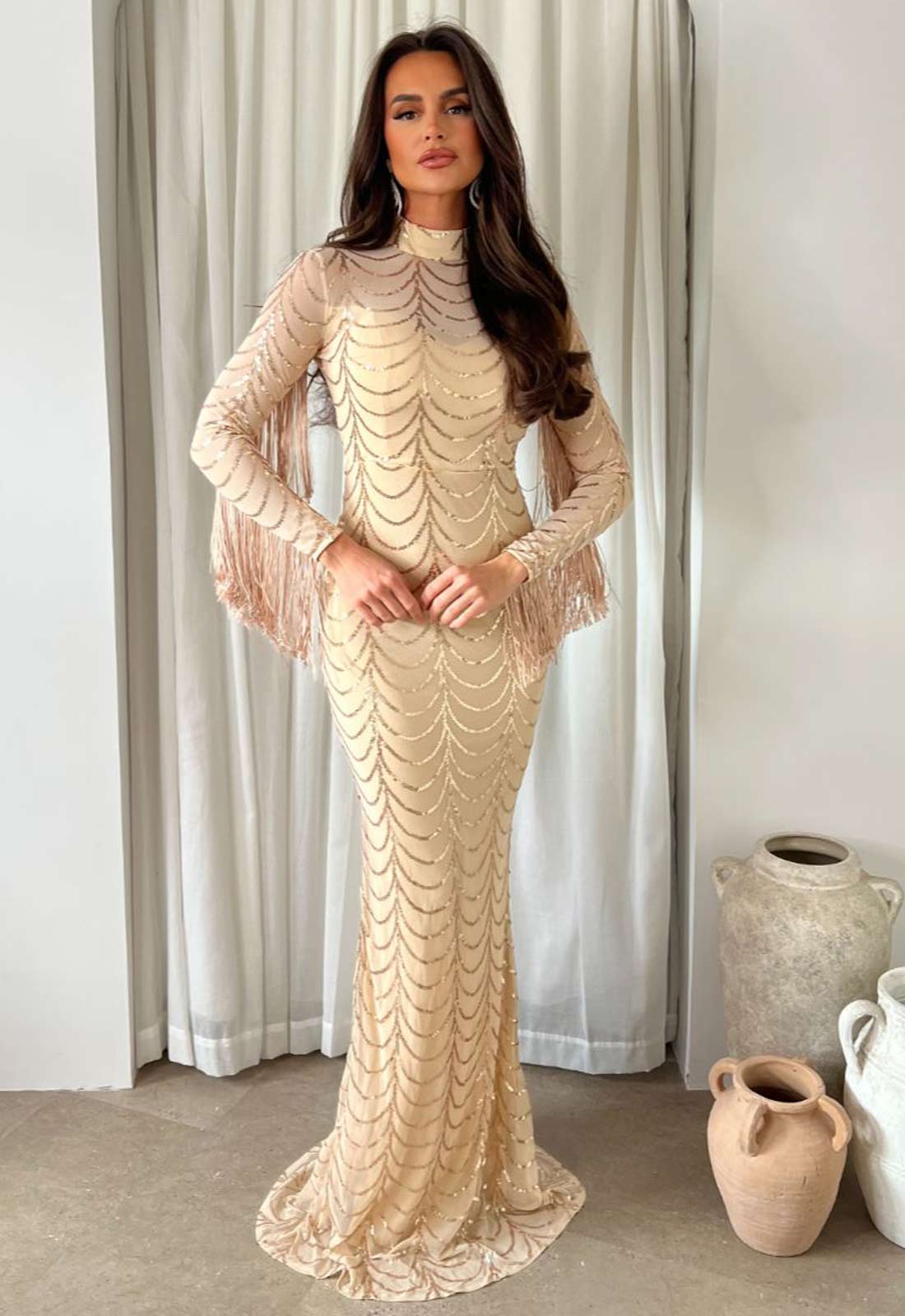 Woman wearing a beige lace dress standing in front of a curtain.