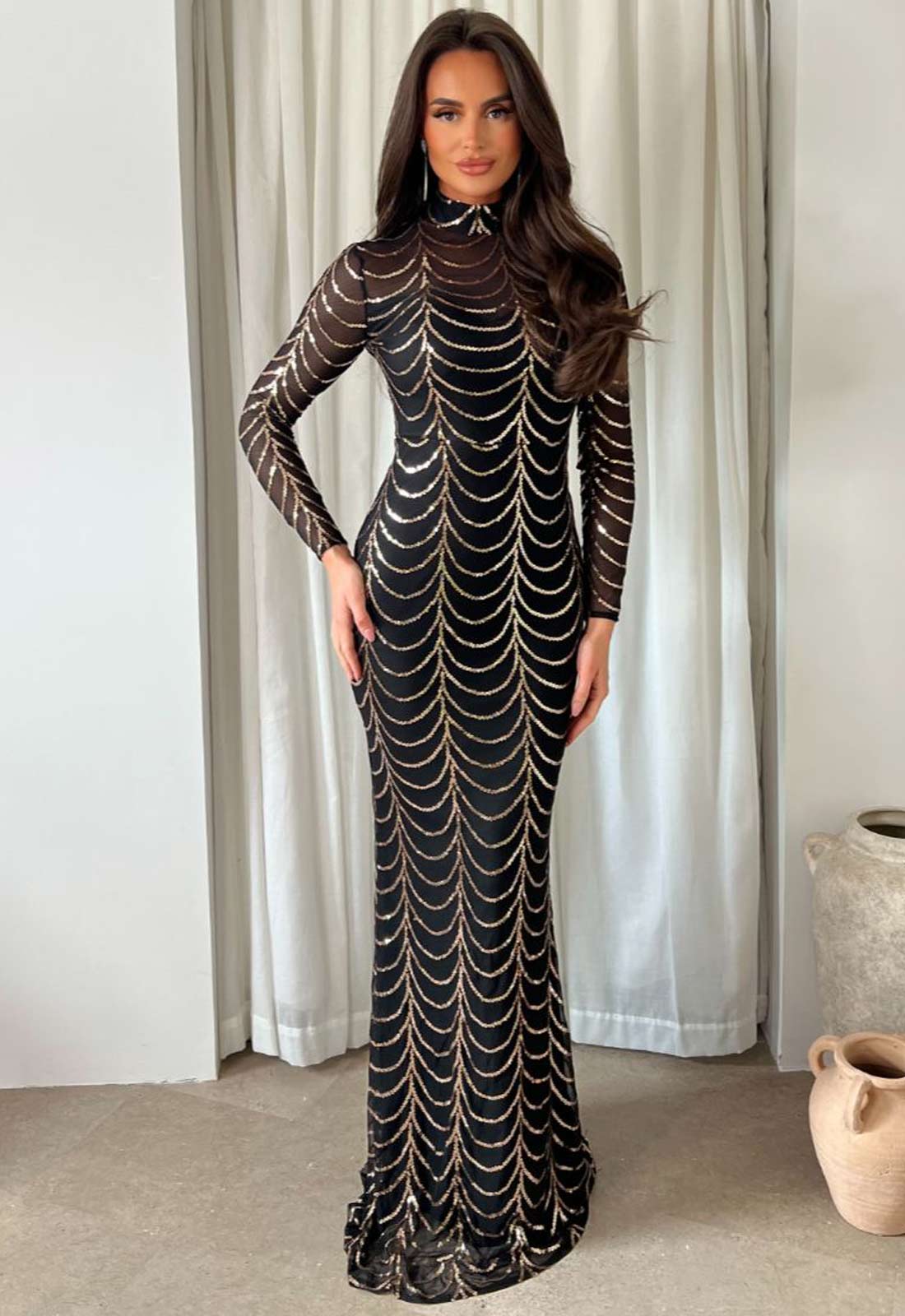Woman wearing a black dress with gold patterns against a white curtain background
