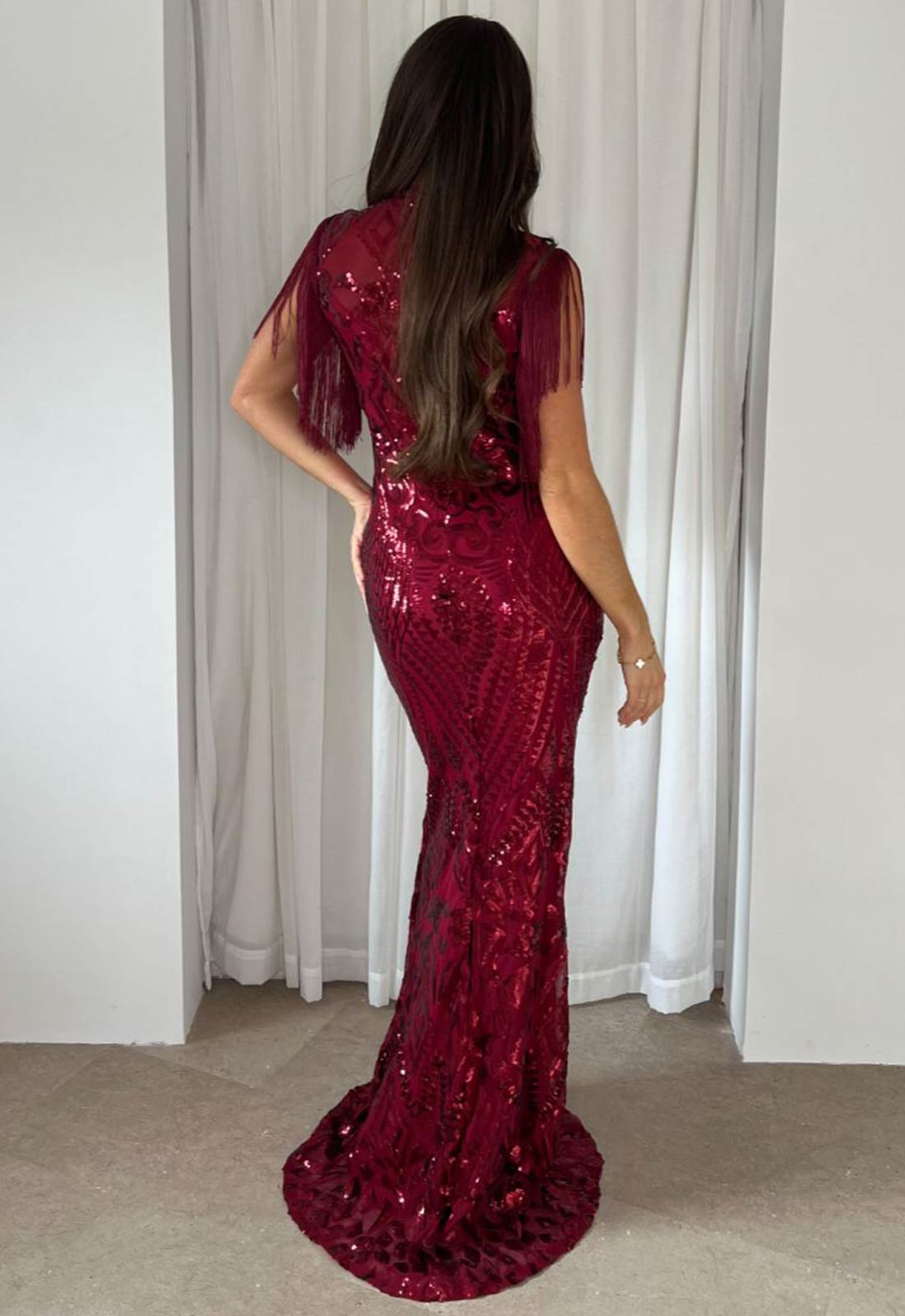 Woman wearing a red sequin dress in front of white curtains