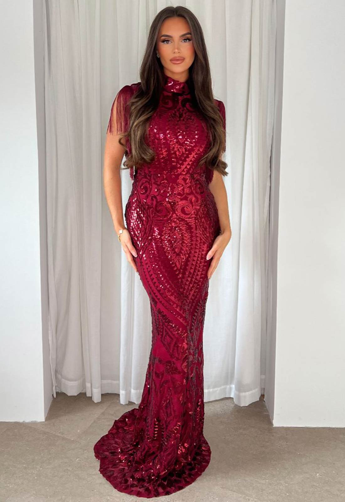 Woman wearing a red sequin dress against a white curtain background